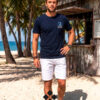 hombre vistiendo camiseta algodón azul marino de La Vespita en kiosko de playa paradisiaca