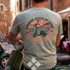 Hombre con camiseta de algodón verde con dibujo en la espalda junto a una moto vespa